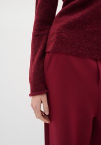 Burgundi neulepaita, jossa on teksturoitu hiha ja rento malli, yhdistettynä vastaaviin burgundin värisiin housuihin, joissa on sivutasku.