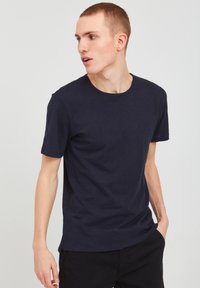 Tricou din bumbac de culoare albastru închis, cu guler rotund și mâneci scurte, având o croială ușor relaxată și o textură netedă.