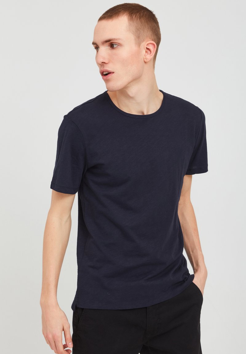Tricou din bumbac de culoare albastru închis, cu guler rotund și mâneci scurte, având o croială ușor relaxată și o textură netedă.