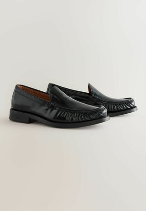 Pantofi loafers din piele neagră, cu vârf rotund, textură pliată în partea din față și toc mic și stivuit. Finisaj neted și design clasic.