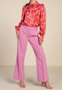 Blouse à motifs floraux rouges avec un col montant et des manches longues, accompagnée d'un pantalon large taille haute rose et de talons aiguilles rose clair.