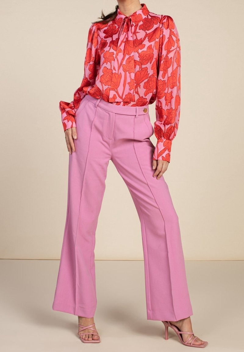 Blouse à motifs floraux rouges avec un col montant et des manches longues, accompagnée d'un pantalon large taille haute rose et de talons aiguilles rose clair.