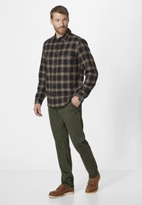 Plaid shirt in navy and brown with button front, two chest pockets, paired with olive green pants and brown lace-up boots.