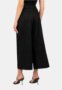 Pantaloni neri a gamba larga realizzati in tessuto liscio, con vita alta, risvolti e tasche laterali. Indossati con tacchi neri a strappo.