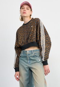 Leopardenmuster-Crop-Sweatshirt mit schwarzen Akzenten. Verfügt über weiße Streifen an den Ärmeln und abgewetzte blaue Jeans, die eine verblasste Textur betonen.