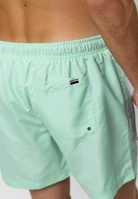 Mentazöld fürdőnadrág, rugalmas derékkal, hátsó zsebbel és kicsi piros, fehér és kék logóval. Simaság és könnyű anyag jellemzi.