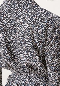 Camicia di tessuto scuro con un motivo di piccoli cuori bianchi, rosa e blu. La texture appare liscia con una leggera lucentezza.