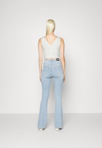 Top cropped cinza claro com costas em V, emparelhado com jeans flared azul claro com dois bolsos traseiros e uma etiqueta na cintura.