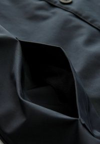 Jant cu un textil negru, cu o textură fină, parțial deschis, dezvăluind un căptușeală moale în interior, pe un fundal al materialului înconjurător.