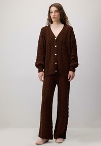 Brown knitted cardigan with cable pattern, featuring large buttons. Paired with matching wide-leg pants. Soft texture and relaxed fit.