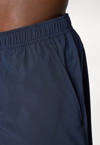 Calças curtas de desporto em azul-marinho, feitas de um tecido suave e leve, com um cós elástico e bolsos laterais. Textura suave, design minimalista.