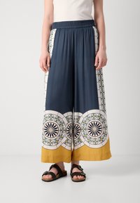Navy and white wide-leg pants with a patterned border featuring circular designs in green, yellow, and blue, finished with a yellow hem.