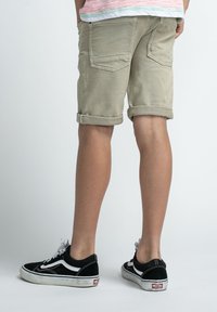 Beige denim shorts met omgeslagen pijpen, voorzien van twee achterzakken. Draagt met zwarte Vans sneakers, die witte accenten en veters laten zien.