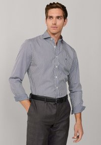 Button-up-paita, jossa on sinivalkoiset pystysuorat raidat, pitkät hihat, kaulus ja hillitty logo. Yhdistetty harmaisiin siippahousuihin ja mustaan vyöhön.