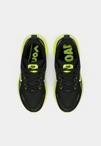 Scarpe da corsa nere con accenti giallo brillante e tomaia in mesh strutturato. Caratteristiche includono lacci, suola ammortizzata e logo del marchio visibile.