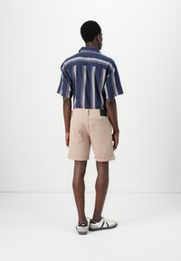 Chemise à rayures bleues à manches courtes et shorts beiges, présentant une coupe décontractée. Les shorts ont des ourlets retournés et des poches arrière, complétés par des baskets.