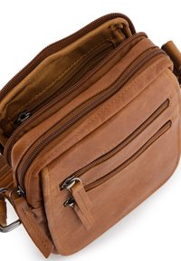 Hnědá kožená crossbody taška s několika zipovými kapsami, texturovaným povrchem a odolným nastavitelným popruhem. Švy jsou viditelné.