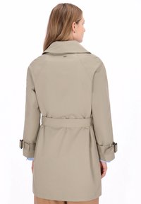 Gabardina beige con cinturón en la cintura, detalles de hombreras y un cuello ancho. Confeccionada en un material suave, con mangas largas y un ajuste entallado.