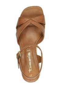 Sandale en cuir marron avec des brides croisées et une sangle à la cheville, présentant une texture lisse et une semelle plate. Détails du logo doré sur la semelle intérieure.