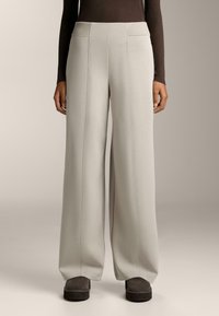 Široke hlače iz svetlo sive tkanine z vidnimi šivi. Imajo visok pas in stranske žepe. Nosi se z temno obutvijo.