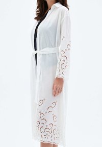 Biała bawełniana szlafrok w stylu kimona z wiązanym w pasie, z misternymi ażurowymi detalami na rękawach i u dołu.