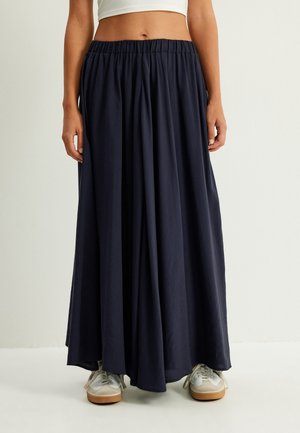 Jupe maxi bleu marine en tissu léger, dotée d'une taille élastique et d'un design fluide, associée à des baskets blanches.