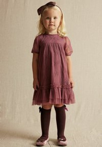 Helles Mauve-Kleid mit durchsichtigen Puffärmeln, Spitzenakzenten und gestuftem Rüschensaum. Kombiniert mit dunkelbraunen knielangen Socken und passenden Schuhen.