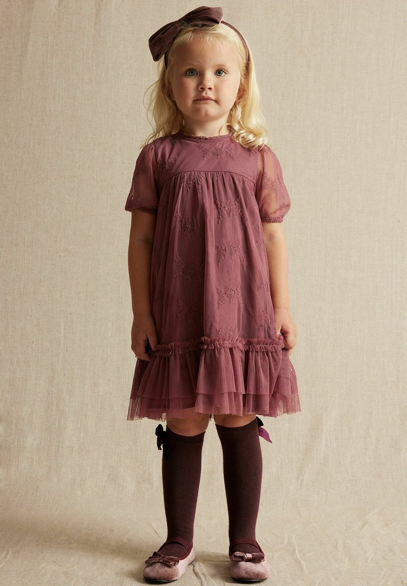 Helles Mauve-Kleid mit durchsichtigen Puffärmeln, Spitzenakzenten und gestuftem Rüschensaum. Kombiniert mit dunkelbraunen knielangen Socken und passenden Schuhen.