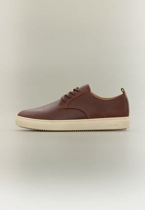Bruine leren lage sneaker met crème rubberen zool en veters, zijbranding en trek lus bij de hiel op een neutrale achtergrond.