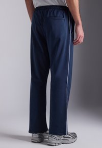 Middengrijze sportieve broek met een ontspannen pasvorm, elastische tailleband en witte zijpaspel. Inclusief een achterzakdetail.