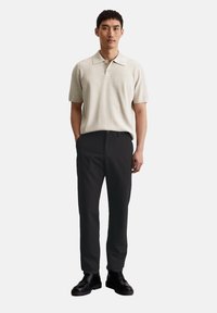 Beige knitted polo shirt with a collar, paired with black slim-fit trousers and black lace-up shoes. Simple design, no visible patterns.