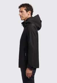 Giacca nera impermeabile con cappuccio, tasca laterale con zip e polsini regolabili. Caratterizzata da una texture liscia e da un design minimalista.