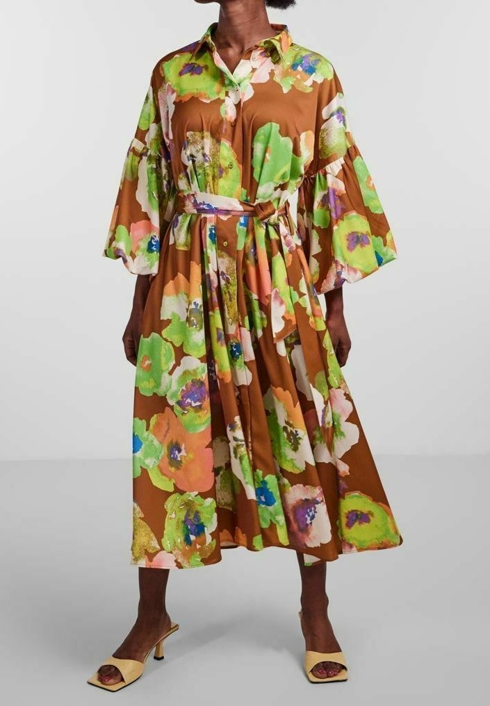 Mujer que lleva un vestido midi marrón con un gran estampado floral colorido, mangas anchas, parte delantera con botones, cinturón atado en la cintura y sandalias beige de tacón.