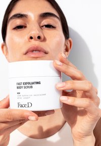 White round jar of "Fast Exfoliating Body Scrub" with black text. Lids are smooth, matte texture; hands are holding it in front of a neutral background.