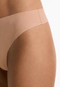 Lichte, naadloze, lage bikini in een nude tint, gemaakt van zachte stof met een gladde textuur en minimale stikdetails.