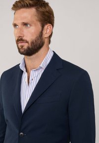 Marineblazer aus strukturiertem Stoff mit einem einzigen Knopfverschluss und Reverskragen, kombiniert mit einem kragenlosen Hemd in Blau-weiß gestreift.