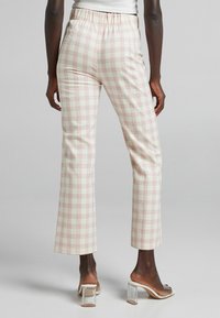 Checked trousers with an elastic waistband, featuring a light cream background and pink plaid pattern, paired with clear heeled mules.
