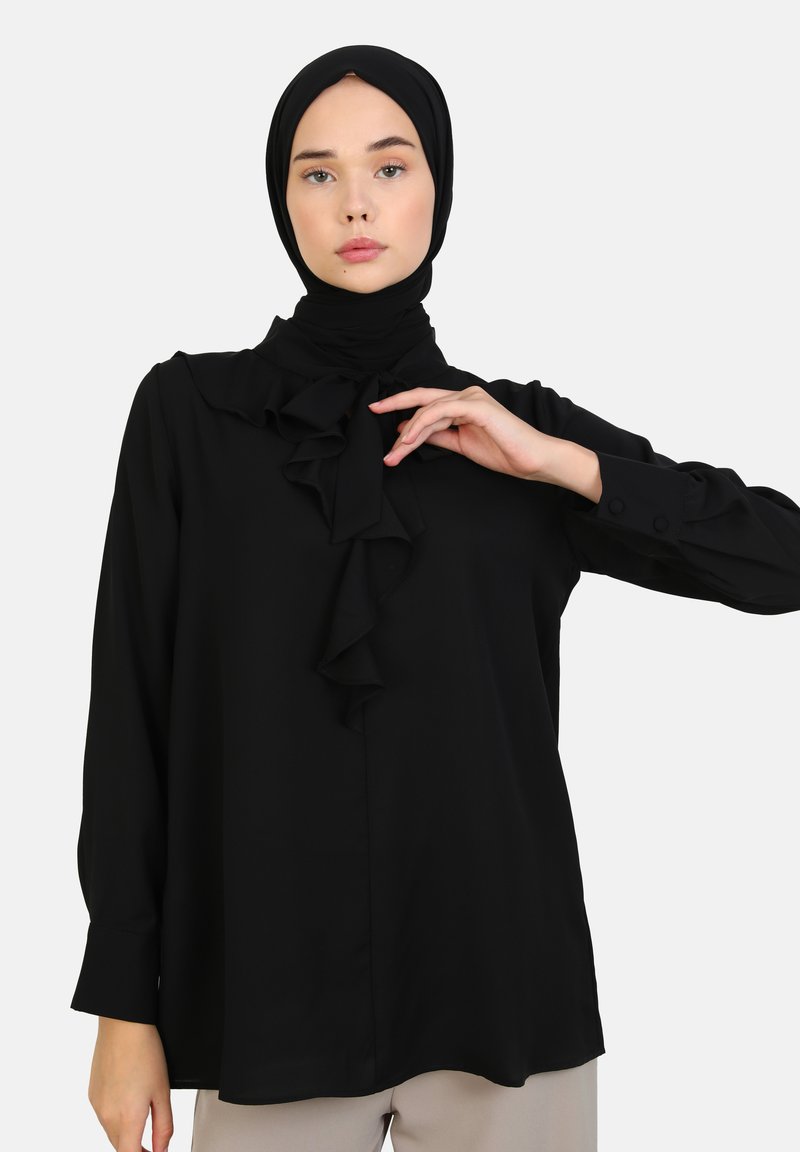Black blouse with a ruffled neckline detail, long sleeves with button cuffs, made from a smooth, lightweight fabric.