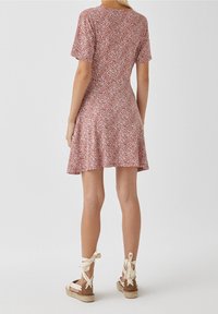 Vestido rojo con estampado floral, de mangas cortas y dobladillo acampanado. Combinado con sandalias de esparto en tono marrón claro, con cintas beige atadas en los tobillos.