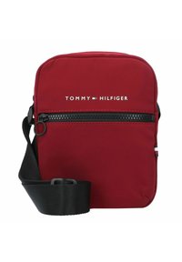 Borsa a tracolla in nylon rosso con tasca frontale con zip, tracolla nera e testo del logo bianco. Presenta accenti orizzontali blu, bianchi e rossi.