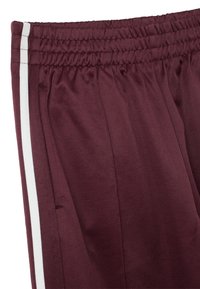 Burgunderfarbene Sporthose mit weißen Seitenstreifen, elastischem Bund und weichem Stoffgefühl. Verfügt über seitliche Taschen und eine lockere Passform.