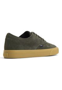 Adidași din suede verde, cu un profil jos, talpă din cauciuc și interior negru. Prezintă șireturi rotunde și un logo mic pe lateral.