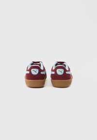 Tenisky Puma s bordó semišovým svrškem, světle modrými akcenty a texturovanou podrážkou z gumy. Kulatý detail loga na patě.