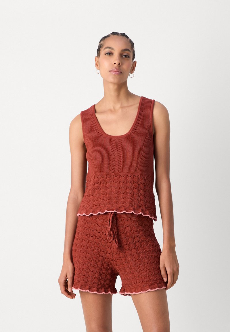 Rostorange Strick-Tanktop mit gewellten Kanten, kombiniert mit passenden Shorts, die ein strukturiertes Muster und einen Kordelzugbund besitzen.