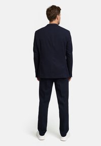 Granatowy garnitur z dopasowaną marynarką i spodniami o gładkiej fakturze. Do tego białe trampki, widok od tyłu.