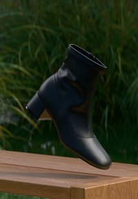 Czarne botki za kostkę o gładkim, błyszczącym wykończeniu, dopasowanym kroju i słupkowym obcasie. Zawierają zaokrąglony czubek oraz elastyczne wykończenie górnej części.