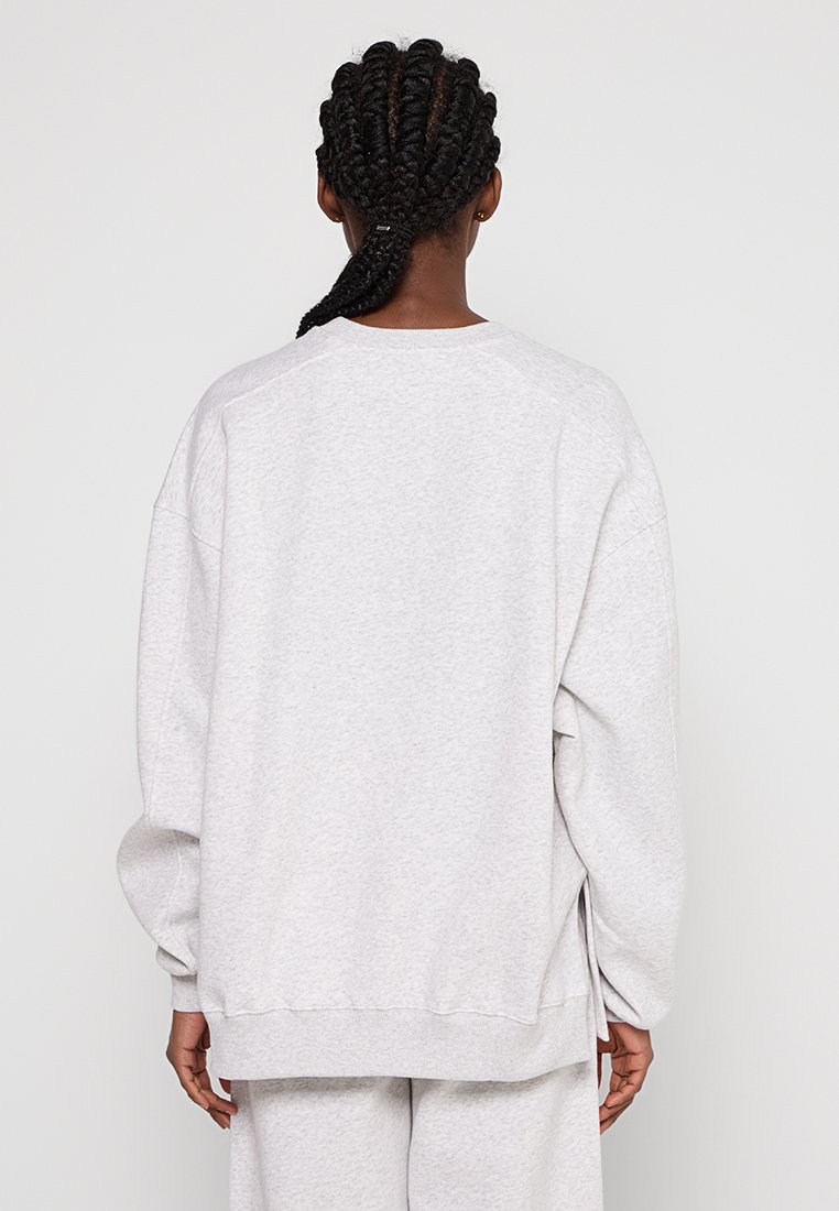 Grau Sweatshirt mit lockerer Passform, überschnittenen Schultern und gerippten Bündchen. Weicher Stoff mit seitlichen Schlitzen und minimaler Markenkennzeichnung auf der Rückseite.
