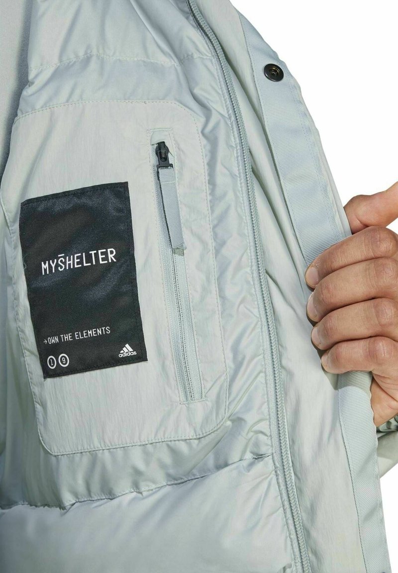 Jasnoszara, ocieplana kurtka z zamkową kieszenią i czarną metką z napisem "MY SHELTER", wykonana z gładkiego, trwałego materiału.