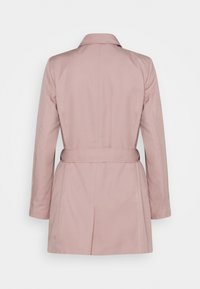 Vaaleanpunainen trenssitakki, jossa on vyötärölle sidottava vyö, pitkät hihat ja jäsennelty kaulus. Sileä kangas, siistit saumat ja räätälöity siluetti.