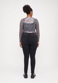 Black high-waisted jeans with a smooth texture, paired with a sheer long-sleeve top featuring a grey leopard print pattern.
